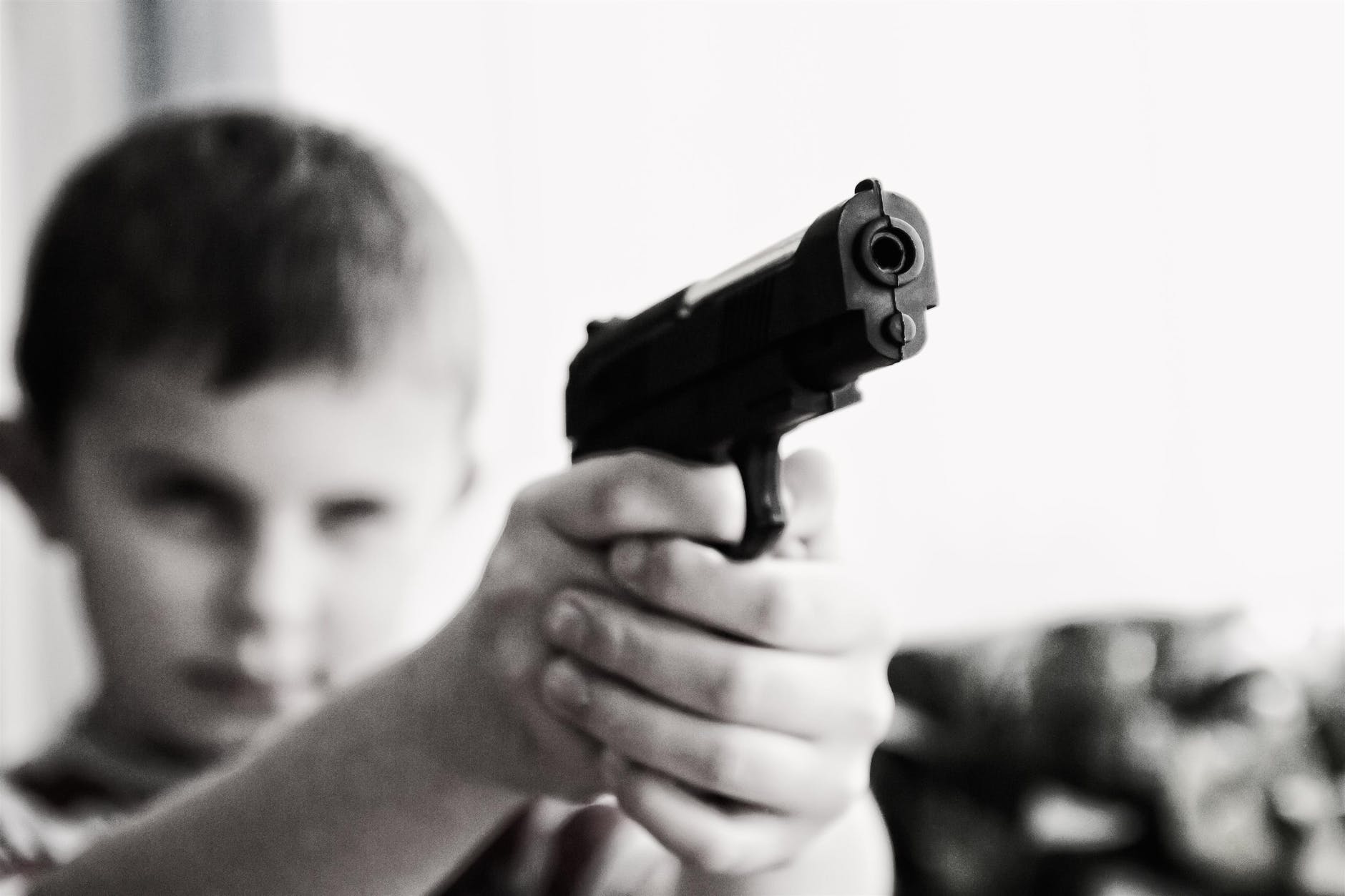grayscale photo of a boy aiming toy gun selective focus photography